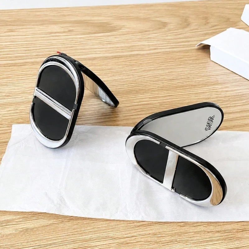 Two oval-shaped black and silver compact mirrors with a glossy finish, displayed on a white tissue paper over a light wood grain surface.